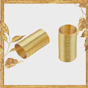May include: Two gold-colored napkin rings. One is lying on its side, and the other is standing upright. The napkin rings are made of tightly wound metal, creating a textured surface. The background is white with a gold border.