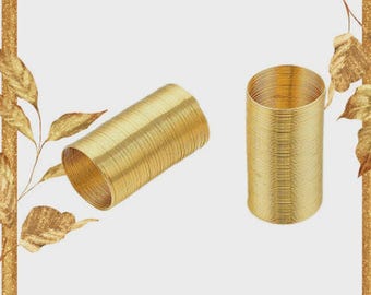 May include: Two gold-colored napkin rings. One is lying on its side, and the other is standing upright. The napkin rings are made of tightly wound metal, creating a textured surface. The background is white with a gold border.