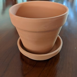 Op de afbeelding: Een terracotta bloempot met een bijpassende schotel. De pot is ongeglazuurd en heeft een natuurlijke bruine kleur.