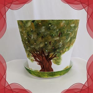 Pode incluir: Um vaso de plantas cónico em cerâmica branca com pires a condizer, apresentando um tronco de árvore castanho pintado à mão e uma copa verde texturizada. A folhagem é decorada com pequenos strass iridescentes espalhados que brilham.