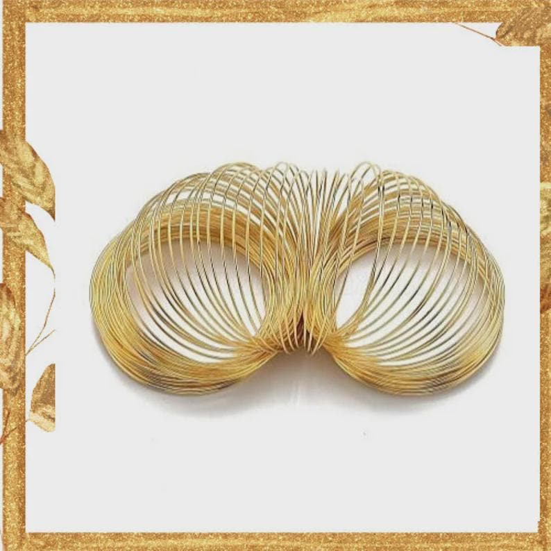 May include: A gold-colored metal spring toy composed of a continuous, tightly coiled wire forming a series of interconnected circular loops. The metallic structure features a reflective finish and is arranged in a horizontal, elongated oval shape.