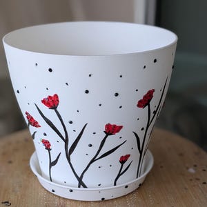 Maceta de plástico de 15 cm de diámetro, pintada a mano y adornada con pedrería, con plato a juego. Pintada con esmalte y detalles de pedrería.