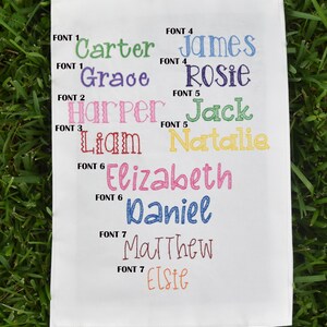 K&ouml;nnte beinhalten: Ein wei&szlig;er Stoffmuster mit verschiedenen Schriftarten und Namen, die in verschiedenen Farben gestickt sind. Die Namen sind Carter, Grace, Harper, Liam, Elizabeth, Daniel, Matthew und Elsie.