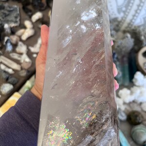 May include: A large, clear quartz crystal point with iridescent inclusions. The crystal is approximately 10 inches tall and has a natural, rough texture.
