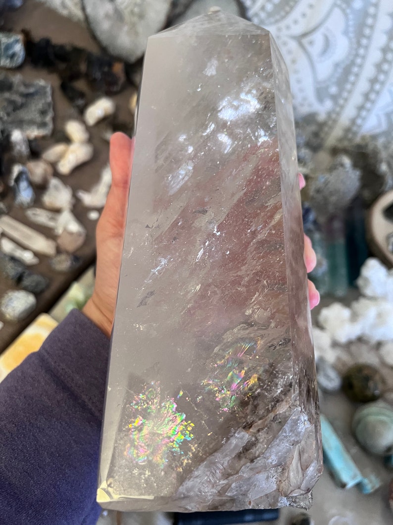 May include: A large, clear quartz crystal point with iridescent inclusions. The crystal is approximately 10 inches tall and has a natural, rough texture.