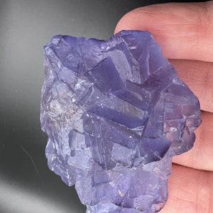 May include: A large, purple fluorite crystal with a rough, textured surface. The crystal has a deep, rich purple color and is composed of many smaller crystals.