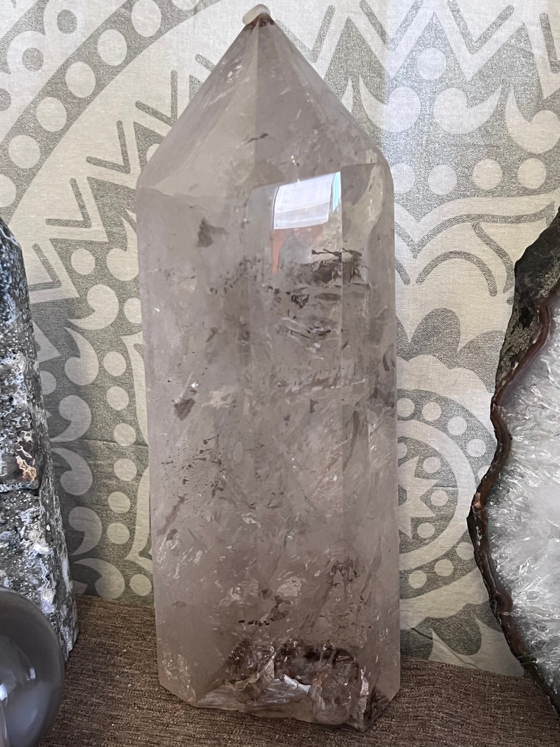 May include: A large, clear quartz crystal point with a natural, rough base. The crystal is translucent and has a slight smoky hue. It is approximately 10 inches tall.