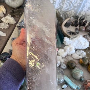 May include: A large, clear quartz crystal point with a slightly pink hue. The crystal is polished and has a smooth, glassy surface. It is a natural crystal and has inclusions and striations.
