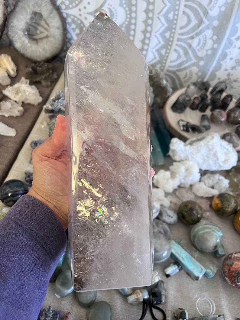 May include: A large, clear quartz crystal point with a slightly pink hue. The crystal is polished and has a smooth, glassy surface. It is a natural crystal and has inclusions and striations.