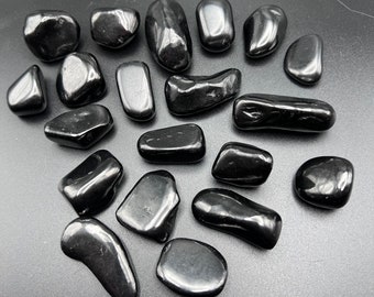 May include: A collection of smooth, black obsidian tumbled stones. The stones are various shapes and sizes, and have a glossy finish.