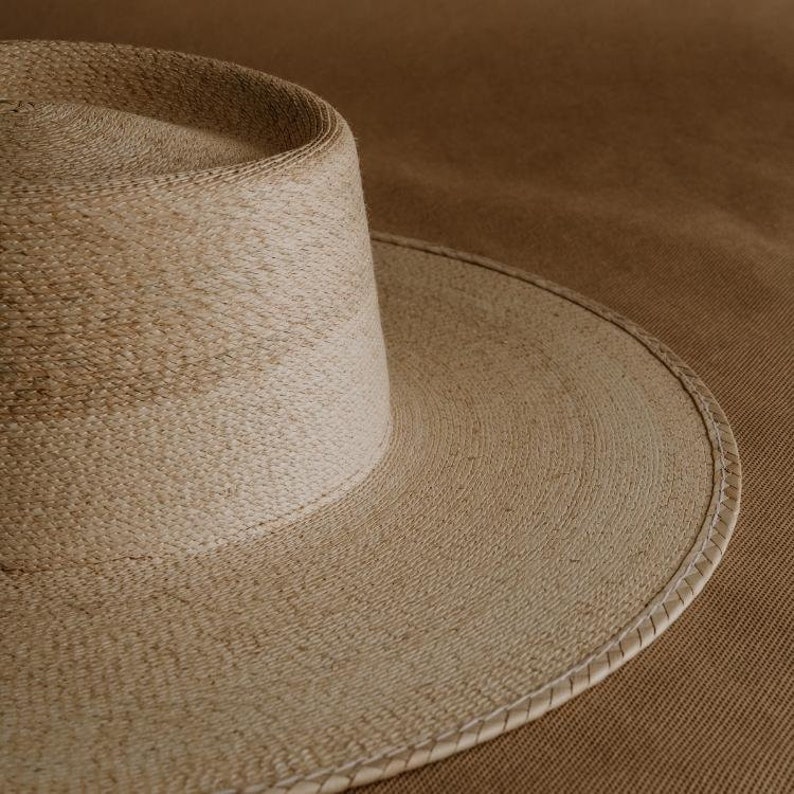 May include: A wide-brimmed straw hat with a light brown color and a stitched edge.