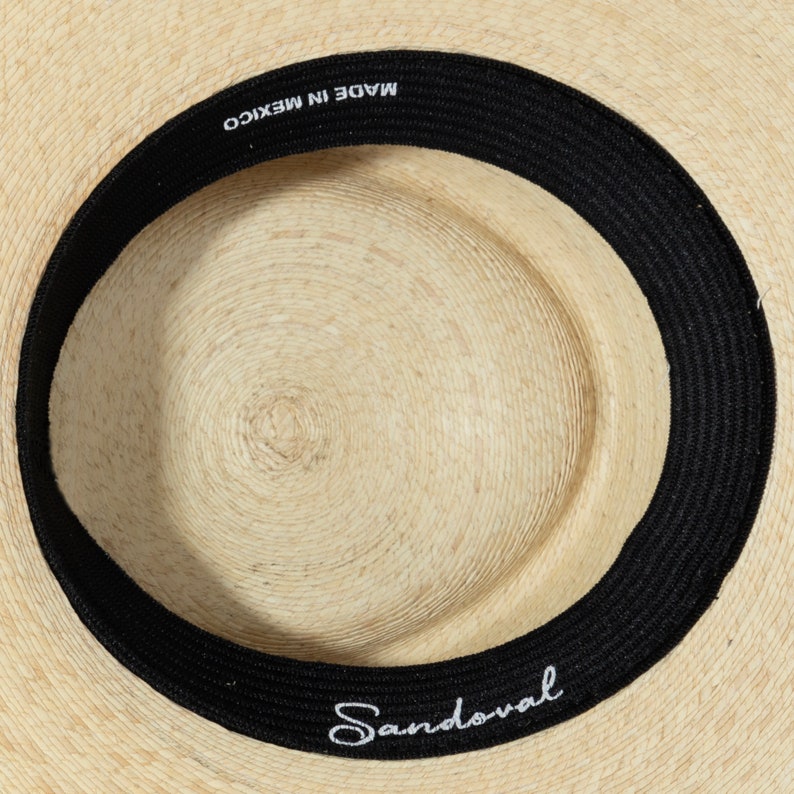 May include: The inside of a straw hat with a black band that says "MADE IN MEXICO" and "Sandoval" in white lettering.