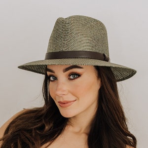 May include: A woman wearing a green and brown woven fedora hat with a brown leather band.