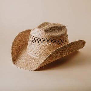 Könnte beinhalten: Ein hellbrauner Strohhut im Cowboy-Stil mit gewebtem Muster und breiter Krempe.