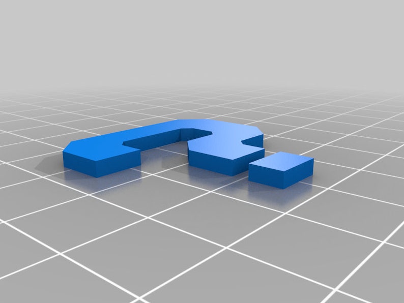 May include: A blue plastic question mark, made up of three separate pieces, is sitting on a gray grid surface.