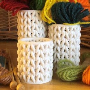 May include: Three white knitted yarn bowls containing balls of yarn in various colours, including red, green, yellow and orange.