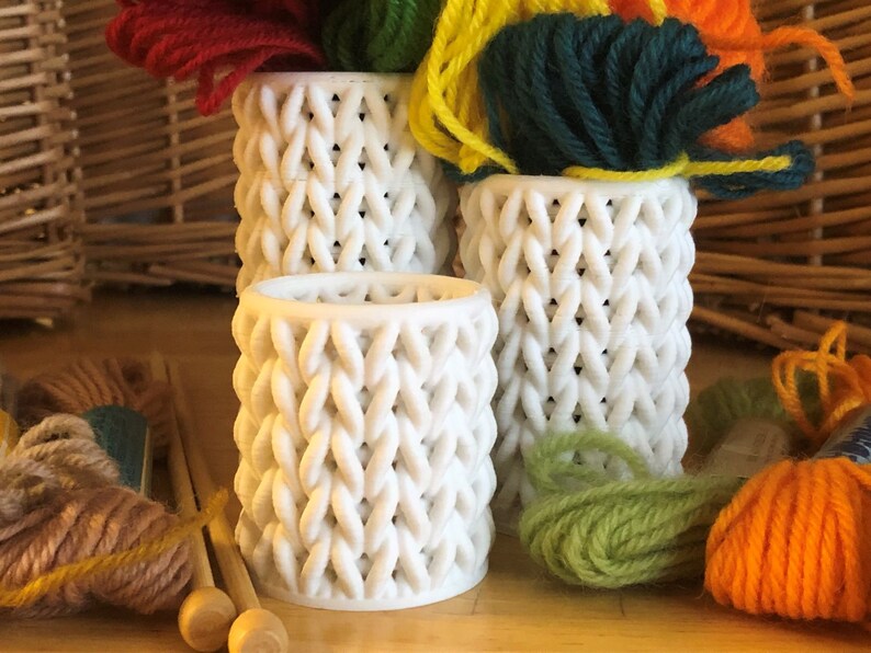 May include: Three white knitted yarn bowls containing balls of yarn in various colours, including red, green, yellow and orange.