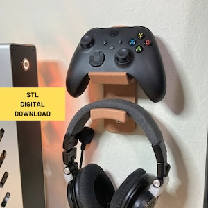 Puede incluir: Un soporte de pared impreso en 3D para un auricular de juego y un mando. El soporte está hecho de plástico marrón y tiene un auricular negro y un mando Xbox negro unidos a él. El texto "STL DIGITAL DOWNLOAD" es visible en la imagen.