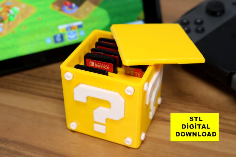 May include: A yellow 3D printed Nintendo Switch game cartridge storage box shaped like a Super Mario Bros. question block with a white question mark on the front. The lid is open and the box is filled with game cartridges. The text "STL DIGITAL DOWNLOAD" is visible in the lower right corner of the image.