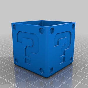 May include: A blue plastic question mark block, similar to the ones found in the Super Mario Bros. video game. The block has a question mark on each side.