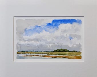May include: Watercolor landscape painting featuring a cloudy sky with blue and gray hues. The foreground depicts a marshy area with brown and green tones, and a distant treeline. The artwork is framed in a white mat.