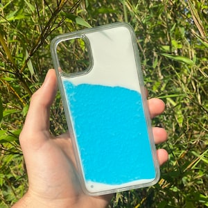 May include: A clear phone case with blue liquid inside. The liquid is moving and creating a wave-like pattern. The case is designed to fit a smartphone with a camera bump.