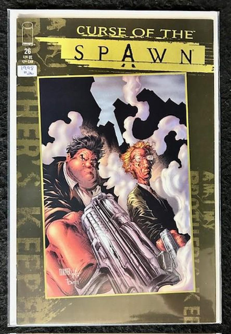 May include: A comic book cover featuring a gold background with the title "Curse of the Spawn" in black and gold lettering. The cover art depicts two men in suits holding a large gun, with smoke and buildings in the background.