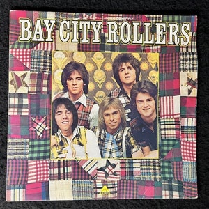 May include: A vintage vinyl record album cover featuring the band Bay City Rollers. The cover features a patchwork quilt design in red, green, yellow, and blue with a white background. The band members are pictured in the center of the cover, wearing plaid shirts and smiling.