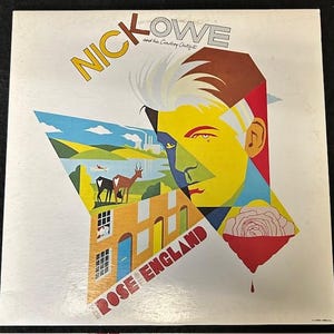 May include: A vintage vinyl record album cover featuring a colorful geometric design with a portrait of Nick Lowe and the text "Nick Lowe and his Cowboy Outfit" and "Rose England".