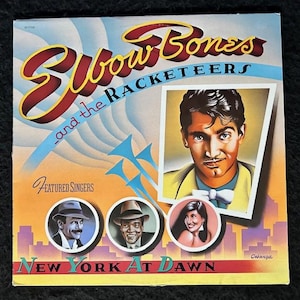 May include: A vintage vinyl record album cover featuring a band called "Elbow Bones and the Racketeers". The album cover is yellow, blue, and red with a photo of a man in a yellow suit and a white bow tie. The album title is "New York at Dawn".
