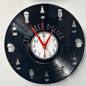 May include: A black vinyl record clock with a white clock face and red hands. The clock features beer bottle and glass silhouettes around the edge. The text "IT'S BEER O'CLOCK" is etched into the vinyl.