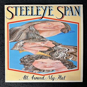以下が含まれることがあります： スティールイ・スパンというバンドのヴィンテージ・レコード・アルバムのカバー。カバーアートは、青い背景に、波打つ髪の3つの顔が描かれたカラフルなイラスト。アルバムのタイトル「All Around My Hat」は、カバーの下部に筆記体で書かれている。