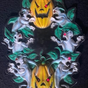 May include: Oval-shaped Halloween decoration featuring two carved pumpkins and four ghostly figures. The pumpkins are yellow with black carved faces and red eyes. The ghosts are white with red eyes and green leaves.