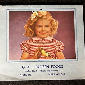 May include: A vintage advertisement for G & L Frozen Foods, featuring a young girl with blonde hair and a white flower in her hair, holding a yellow canary bird. The text reads "Miss Brown Eyes", "G & L Frozen Foods", "Locker Plant - Meats and Groceries", "Phone 148", and "Gull Lake, Sask."