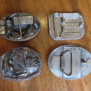 Op de afbeelding: Vier zilveren gespen met verschillende ontwerpen. De gespen zijn ovaalvormig en hebben een metalen sluiting. De gespen zijn allemaal van verschillende grootte en hebben verschillende details.
