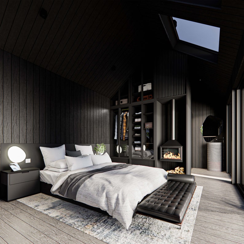Interior view of a studio cabin featuring a cozy chimney, closet, vanity area, and stylish low-profile bed. Light gray flooring contrasts with dark wood walls. Skylights invite natural light, creating a warm, modern cabin aesthetic.