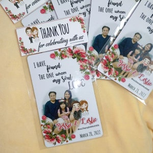 May include: Wedding favour cards featuring a family photo and the text "I have found the one whom my soul loves." The cards are decorated with floral accents and the names "Jessie & Leslie" and the date March 28, 2022.
