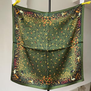 May include: A square silk scarf in olive green featuring a detailed botanical and animal print. The design includes various birds, small creatures, and floral elements scattered across the centre, framed by a dark border with red accents.