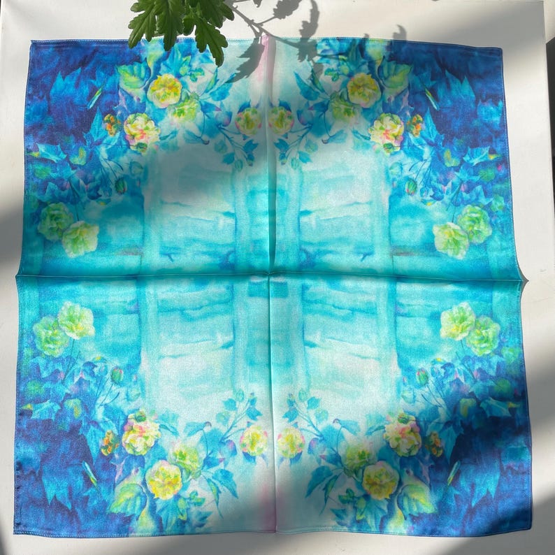 K&ouml;nnte beinhalten: Ein quadratisches Seidentuch mit einem lebendigen Aquarelldruck aus gelben und gr&uuml;nen Blumen vor einem Farbverlauf, der von tiefem Marineblau an den R&auml;ndern zu hellem T&uuml;rkis und Hellblau in der Mitte &uuml;bergeht.