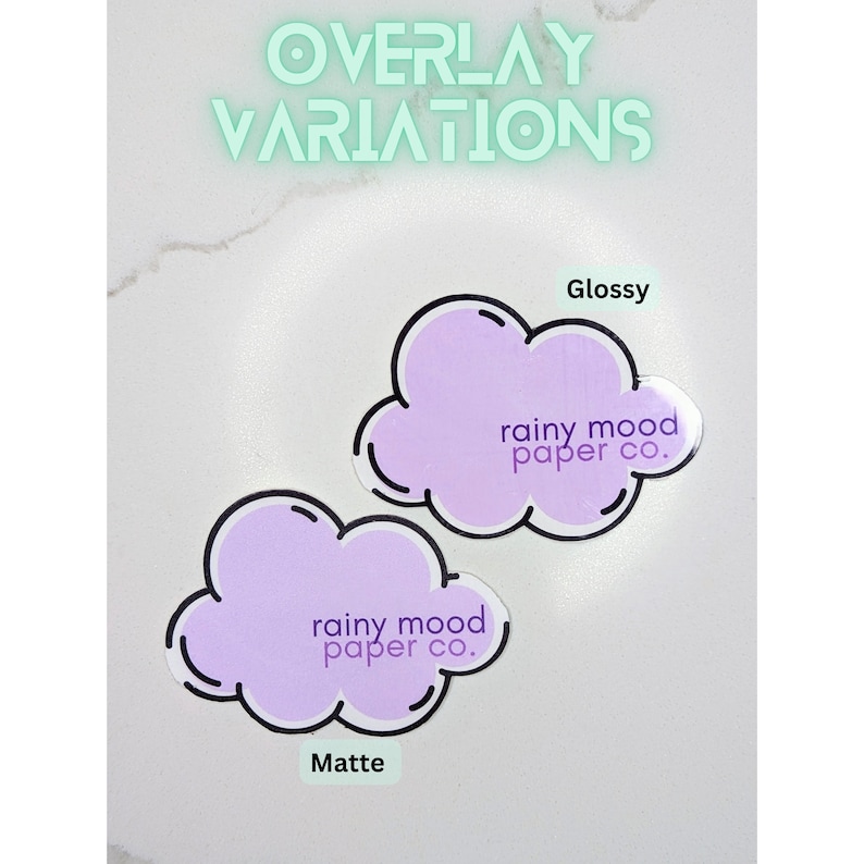 May include: Two purple cloud-shaped stickers with the text "rainy mood paper co." in black text. The sticker on the left has a matte finish and the sticker on the right has a glossy finish.
