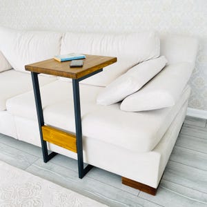 May include: A wooden side table with a black metal frame. The table has a rectangular top and a shelf underneath. The table is next to a white couch.