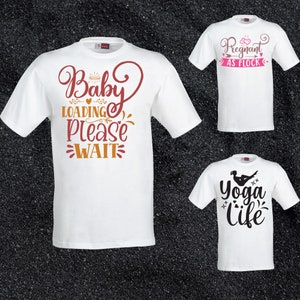May include: Three white t-shirts with different designs. The first shirt has the text "Baby Loading Please Wait" in brown and orange. The second shirt has the text "Pregnant as Flock" in pink and brown. The third shirt has the text "Yoga Life" in black with a silhouette of a person doing yoga.