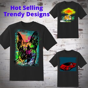 May include: Three black t-shirts with different colorful graphic designs. The first shirt features a colorful German Shepherd dog, the second shirt features a yellow camper van in a forest setting with the text "Happy Campers", and the third shirt features a red sports car on a blue background.