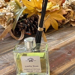 Puede incluir: Una botella de vidrio transparente con una tapa plateada y una etiqueta que dice "section -26- Vanilla Bean Difusor arom&aacute;tico - Hecho a mano Base org&aacute;nica | 4 fl oz".