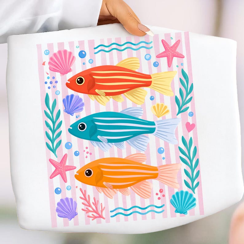 Pu&ograve; includere: Borsa tote bianca con un design acquatico colorato. Il design include tre pesci a strisce in rosso, blu e arancione, circondati da conchiglie, stelle marine e bolle. Sfondo a righe rosa e bianche.