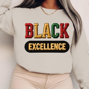 Puede incluir: Una sudadera color crema con las palabras "BLACK EXCELLENCE" bordadas en rojo, dorado y verde. Debajo, un óvalo negro muestra "EXCELLENCE" bordado en dorado.
