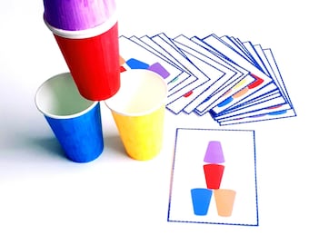 Puede incluir: Un conjunto de vasos coloridos apilados uno encima del otro. Los vasos son rojo, azul, amarillo y morado. También hay tarjetas con imágenes de los vasos.