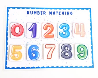 May include: A colorful educational toy for kids featuring a number matching game. The game includes ten colorful squares with numbers 0 through 9 printed on them. The squares are arranged in two rows of five. The game is titled "NUMBER MATCHING".