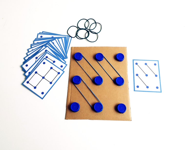 May include: A handmade educational toy featuring a cardboard base with blue bottle caps and rubber bands. Includes a set of blue-bordered cards with dot patterns and a collection of black rubber bands. The toy is designed for learning and play.