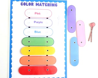 May include: A color matching game for kids. The game features a rainbow xylophone with six bars and a set of loose pieces that match the colors of the xylophone. The game is labeled "COLOR MATCHING" at the top.